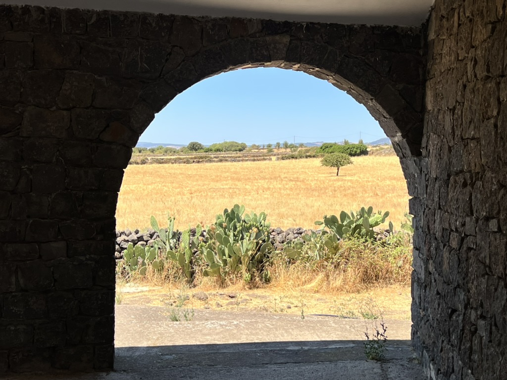Old stone arch framing a dry Sardinian field